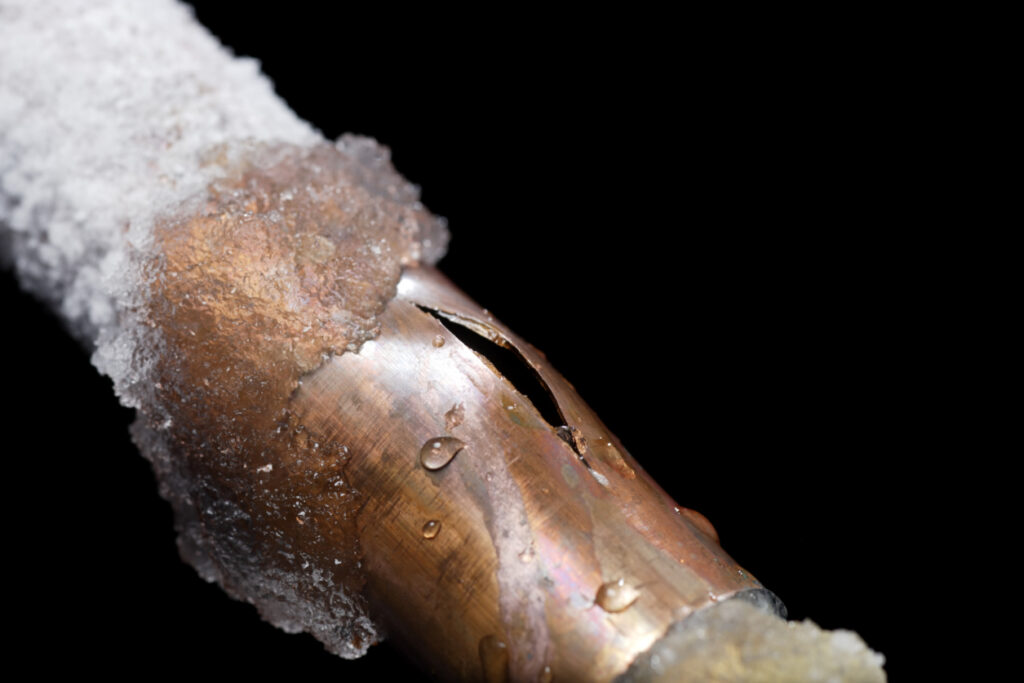 Frozen, cracked copper pipe with ice formation.